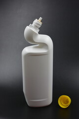 A white plastic bottle with a curved neck and a yellow cap is placed on a black plastic background....