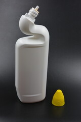 A white plastic bottle with a curved neck and a yellow cap is placed on a black plastic background....