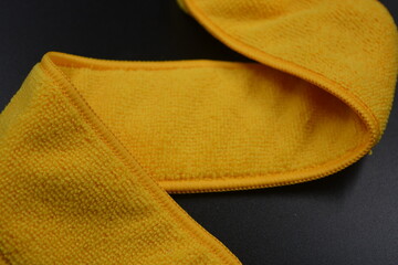 An unusual cleaning cloth, a long yellow microfiber set on a black, matte plastic background.