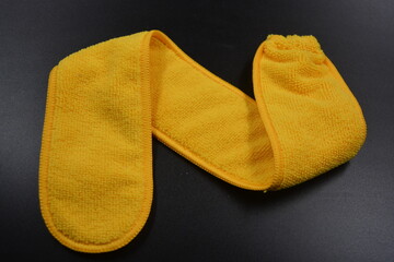 An unusual cleaning cloth, a long yellow microfiber set on a black, matte plastic background.