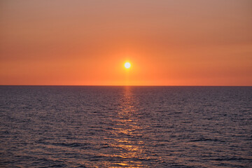 Fototapeta premium Panorama of sea sunrise, ocean sunrise, seascape. Romantic colorful sunset at the sea. The sun touches horizon. Bright sunset with large yellow sun under the sea surface.