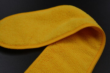 An unusual cleaning cloth, a long yellow microfiber set on a black, matte plastic background.