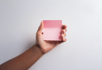 A hand holds a pink square sticky note against a white background.