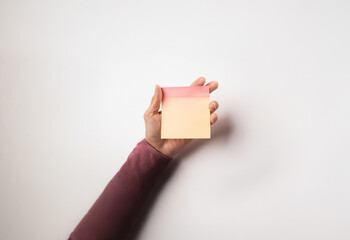 A hand holds a blank yellow and pink sticky note against a white background.