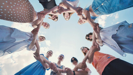 Group of young students are standing in a circle, holding hands and looking up at the sky.