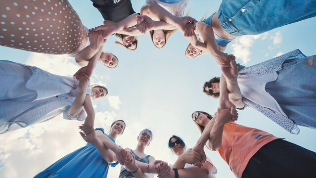 Group of young students are standing in a circle, holding hands and looking up at the sky.