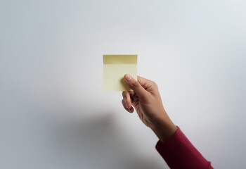 A hand holding a blank yellow sticky note against a white background.