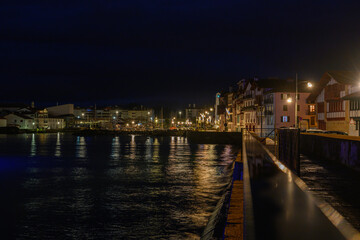 Saint Jean de Luz, France, in the solitude of the night at an almost dark harbor under the blue glow of streetlights. From the promenade, the city begins to awaken in the very early hours of the morni