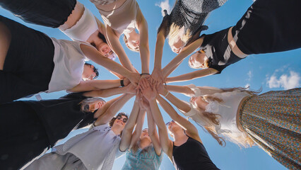 High school students joining hands in a circle under a clear blue sky, symbolizing unity, teamwork,...