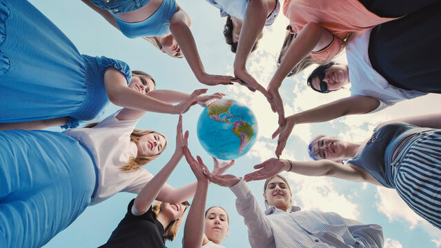 Group of young friends forming a circle with their hands around a globe against a blue sky, symbolizing their commitment to environmental protection