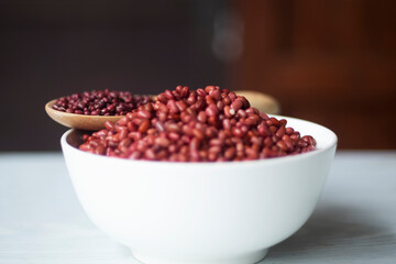 Azuki or Adzuki beans (Japanese red bean or red mung bean) after soaked in white bowl and dried before soaked in wooden spoon isolated on a table closed up. Selective focus blur background
