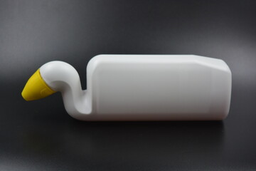 A white plastic bottle with a curved neck and a yellow cap is placed on a black plastic background....