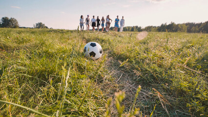 Soccer ball is lying on grass while female soccer school players are walking on field after match.