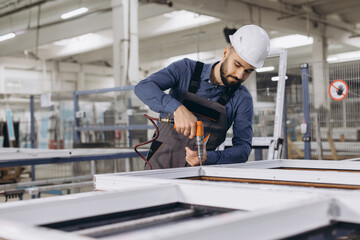 Factory worker assembling aluminum and PVC window frame using electric screwdriver