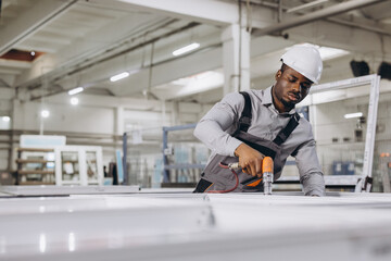 Factory worker assembling aluminum window frames using pneumatic screwdriver