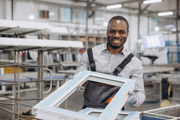Factory worker holding aluminum window frame, smiling at camera