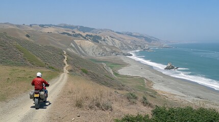 Obraz premium A motorcyclist rides along a scenic coastal dirt road with ocean views.