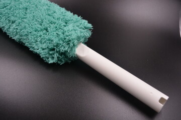 Beautiful green soft fluffy, nylon, synthetic fabric with white plastic base, handle for cleaning and cleaning the room from dust is located on a black plastic background.