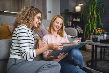 Two female friends looking at an old photo album at home