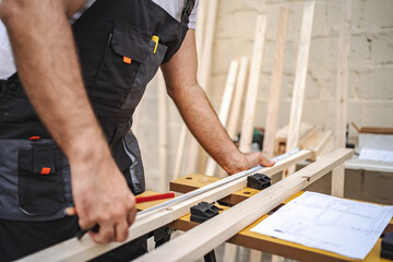 Unrecognizable men measuring wooden plank outdoors