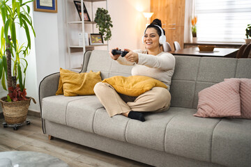 Woman with wireless headphones having fun playing video games at home