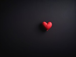 a small, red, heart-shaped object placed against a plain black background. The heart is positioned slightly off-center towards the right side of the image