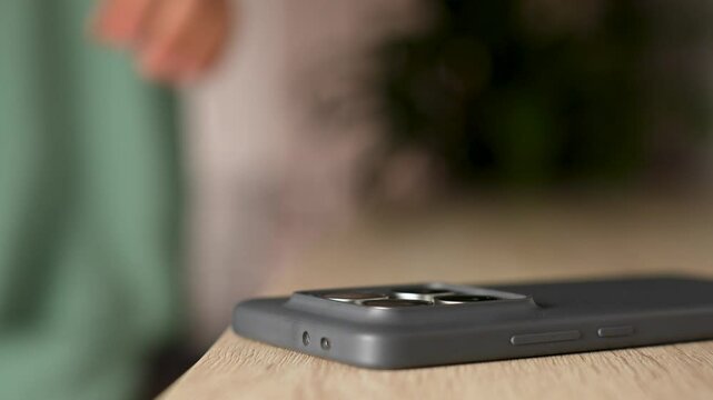 Woman picking up smartphone on her way out. Close-up of woman hand taking a mobile phone from a wooden table