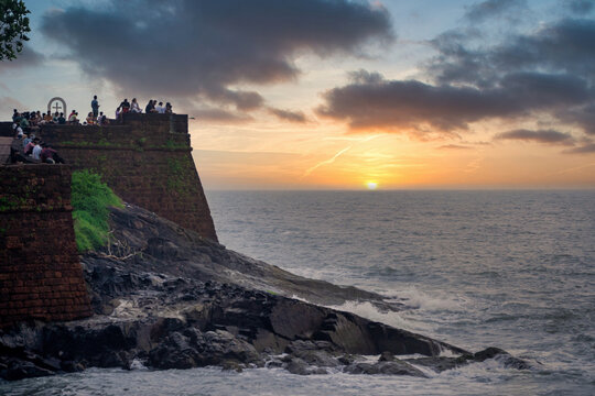 Zoomed in shot of tourists enjoying the view at Sinquerim Aguada fort with high monsoon waves at dusk splashing against the huge stone walls of the tower in goa Maharashtra