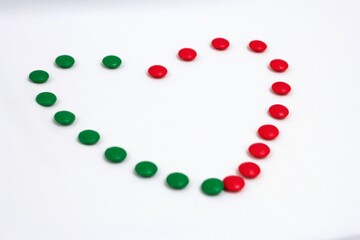 Heart shape made of green and red circular candies on a clean white background, symbolizing love, harmony, and festive themes