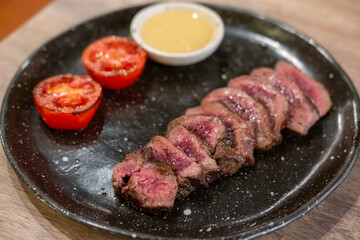 Medium rare striploin steak served on plate with tomato and lemon