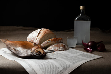 Still life of traditional Eastern European food featuring a glass and carafe of vodka, smoked fish,...