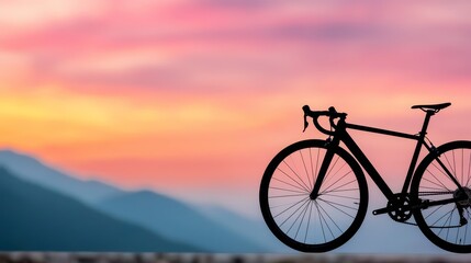Fototapeta premium A bicycle is silhouetted against a sunset sky with mountains in the background