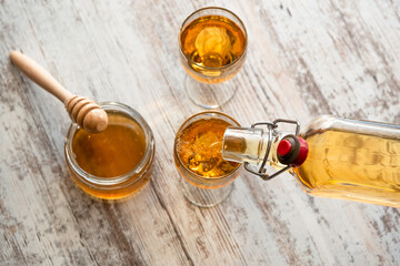 Still life close-up of two glasses of honey mead (medovukha) with honey dipper on wooden surface, dramatic side light
