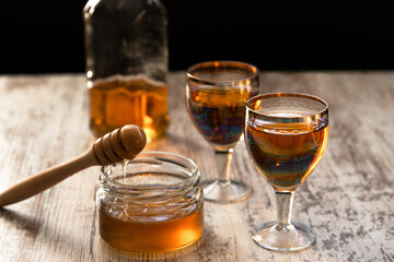Still life close-up of two glasses of honey mead (medovukha) with honey dipper on wooden surface, dramatic side light