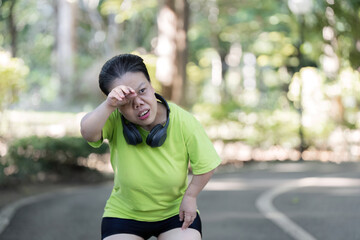 Exhausted Woman Jogging in Park with Headphones, Taking a Break on a Sunny Day