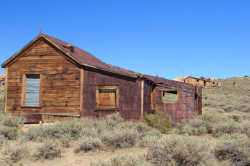 A rustic old house with a tin roof sits in a desert