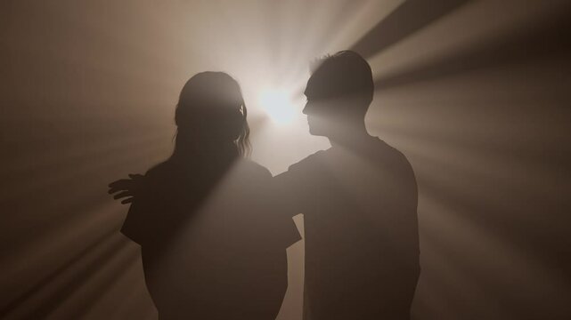 Silhouettes of man and woman hugging and walking towards camera against bright warm colored spotlight, isolated on studio background close up shot.