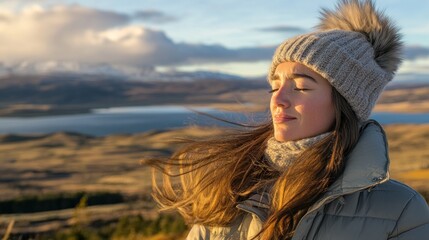 Serene young woman breathes fresh air on a mountaintop at sunset.