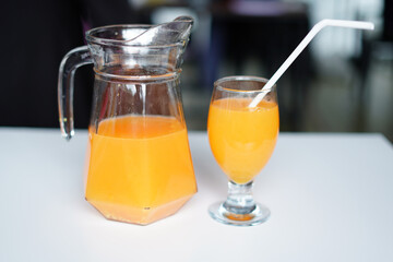 Orange Fruit Juice in Glass Jug and Glass with white straw. on the white table Vibrant Stock Photo