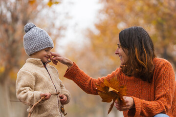 Mother playfully touching her child's nose in a park during autumn. Estilo de vida, Motherhood.