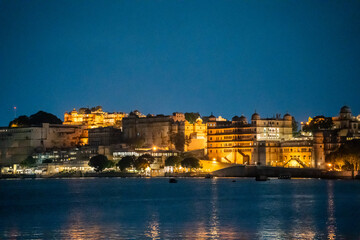 Obraz premium Evening dusk shot of Udaipur city palace on lake pichola lit up with lights reflecting in the water a popular tourist attraction