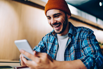 Overjoyed male in hat surprised with victory in online competition in social networks getting...