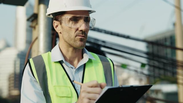 Portrait of man engineer in hardhat tracking project milestones standing on construction site. Male contractor in reflective vest writes down ideas for adjustments looking away
