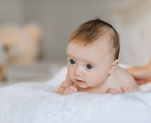 A baby is laying on a white blanket with its head tilted to the side. The baby's eyes are closed,...