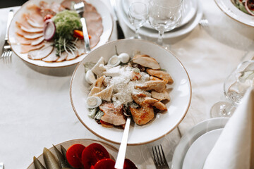 A table with a white tablecloth and a variety of food, including a white plate with chicken and cheese