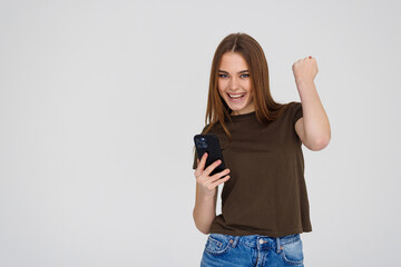 Portrait of a happy joyful woman holding mobile phone and celebrating a win isolated over white background