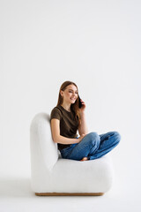 Young woman talk on mobile cell phone sits in armchair on white background