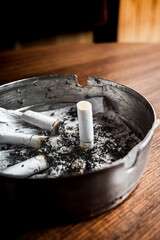 Burnt cigarettes in an ashtray on a wooden table with wet tissue inside	