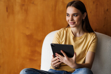 Happy woman sitting in armchair with tablet , studying remotely or having online meeting