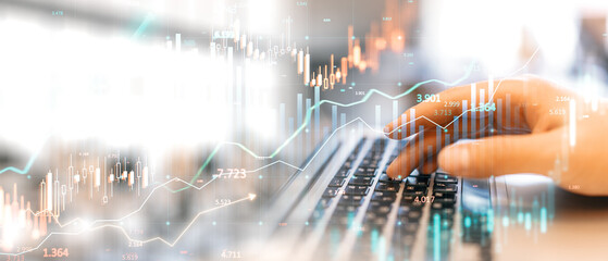 Hands typing on laptop keyboard with overlay of financial graphs and candlestick charts.